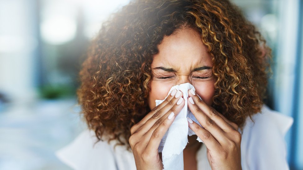 Una mujer se cubre la nariz con un pañuelo al estornudar