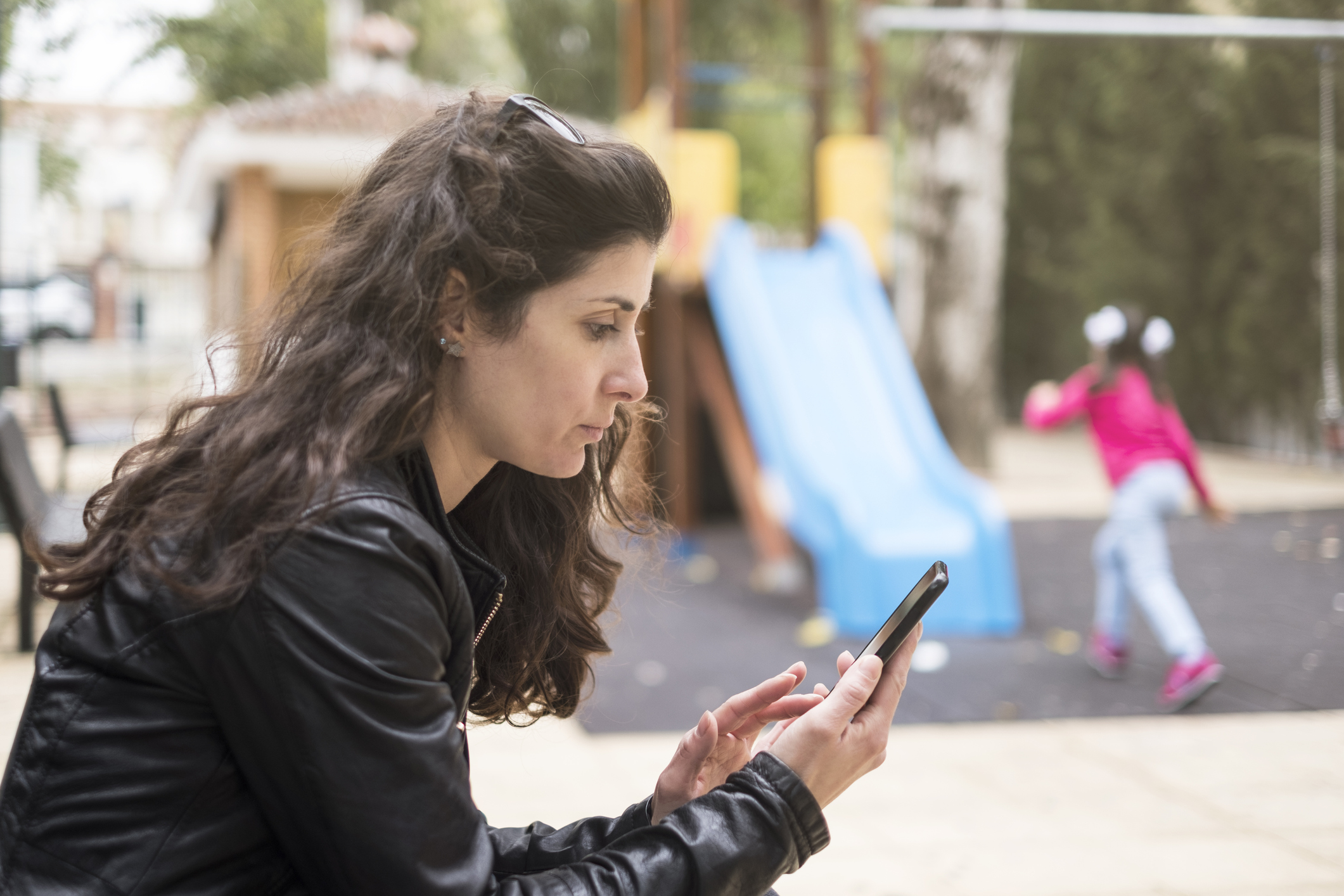 Mãe distraída no telefone enquanto a filha brinca no parque