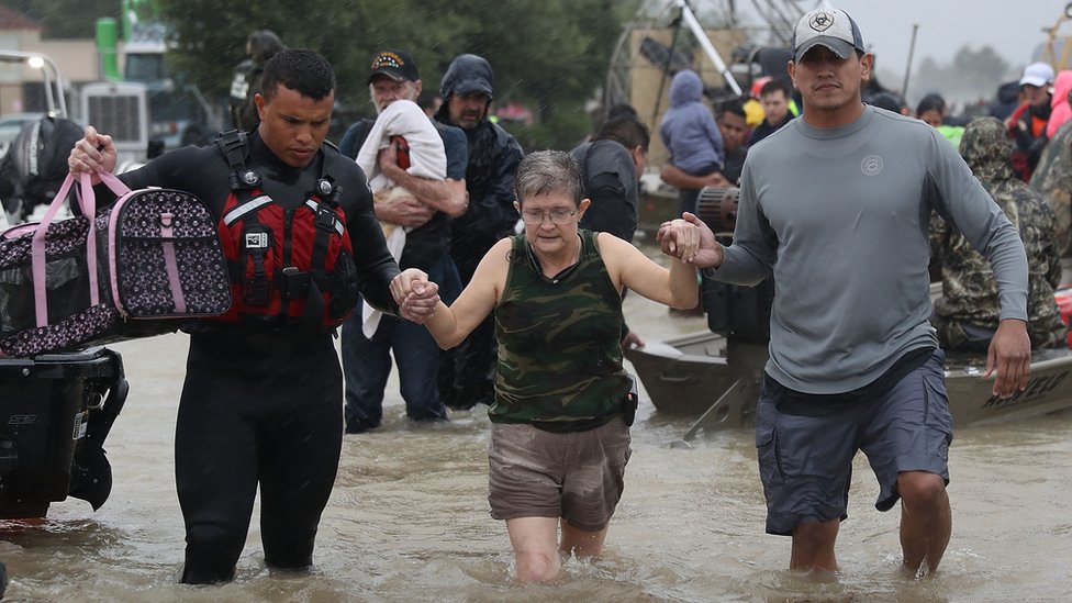 После урагана Харви женщину ведут через паводковые воды в безопасное место