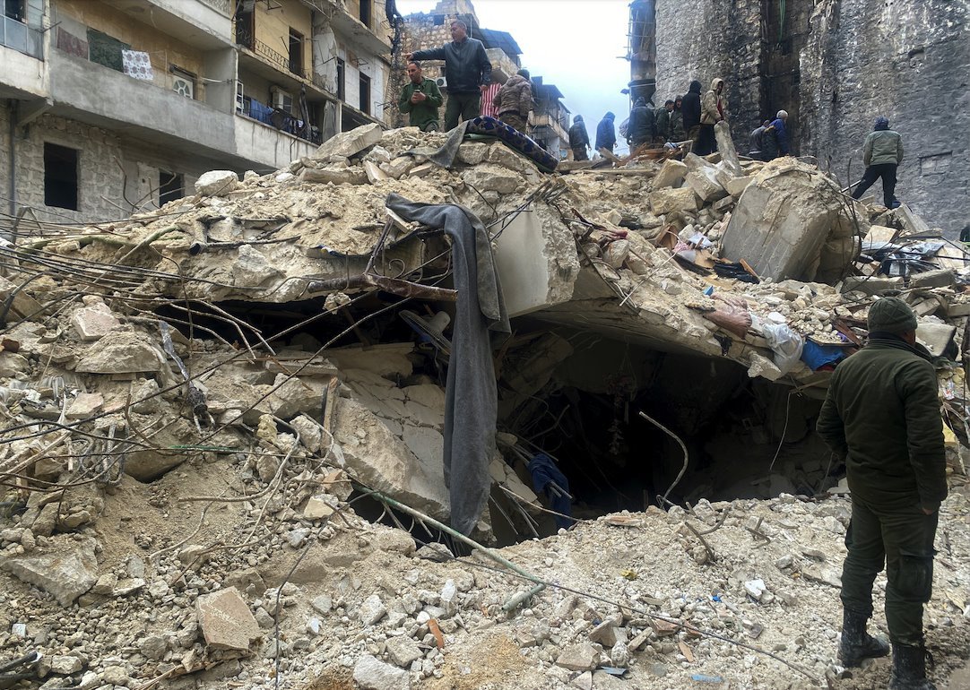 A collapsed building with people standing on the rubble