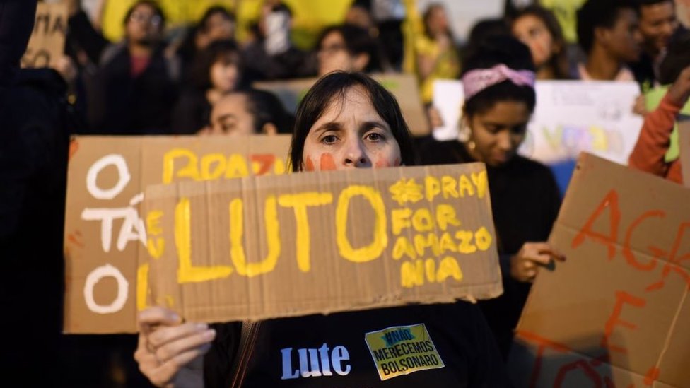 Manifestante com cartaz em protesto pela Amazônia em que se lê: luto, rezem pela Amazônia