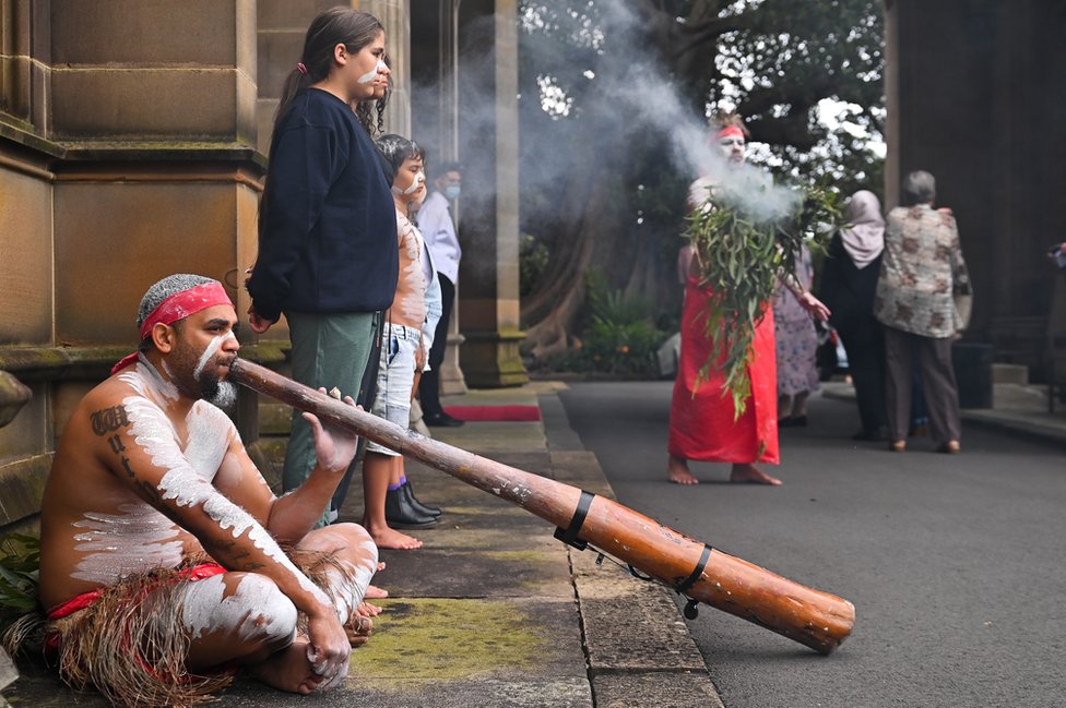 Celebrations of the accession in Sydney, Australia, including an Aboriginal smoking ceremony and man playing a didgeridoo