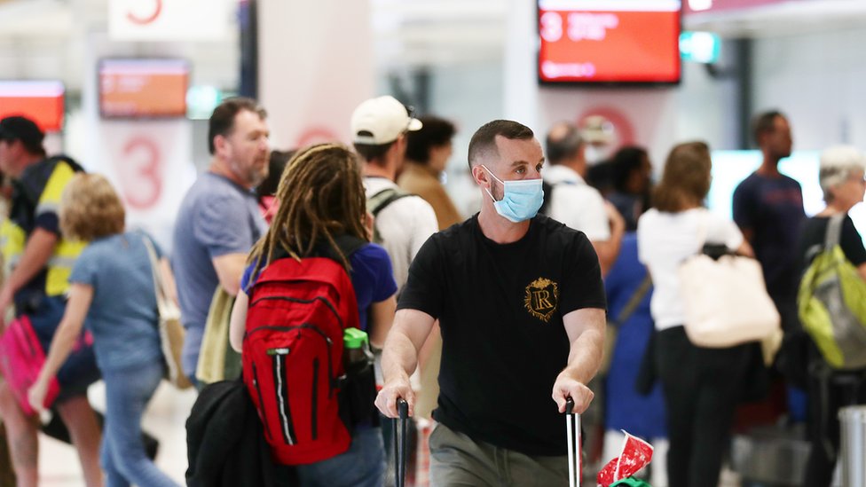 Путешественник, прибывающий из Мельбурна, в маске возит багаж через толпу во внутреннем аэропорту Сиднея 2 июля 2020 года