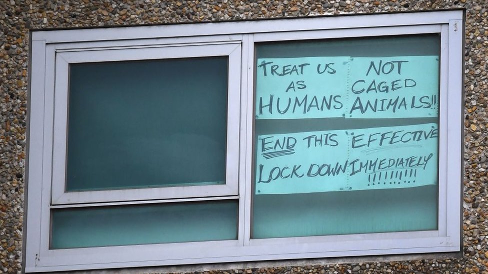 Табличка в окне одного из запертых помещений гласит: «Обращайтесь как с людьми, а не как с животными в клетке»