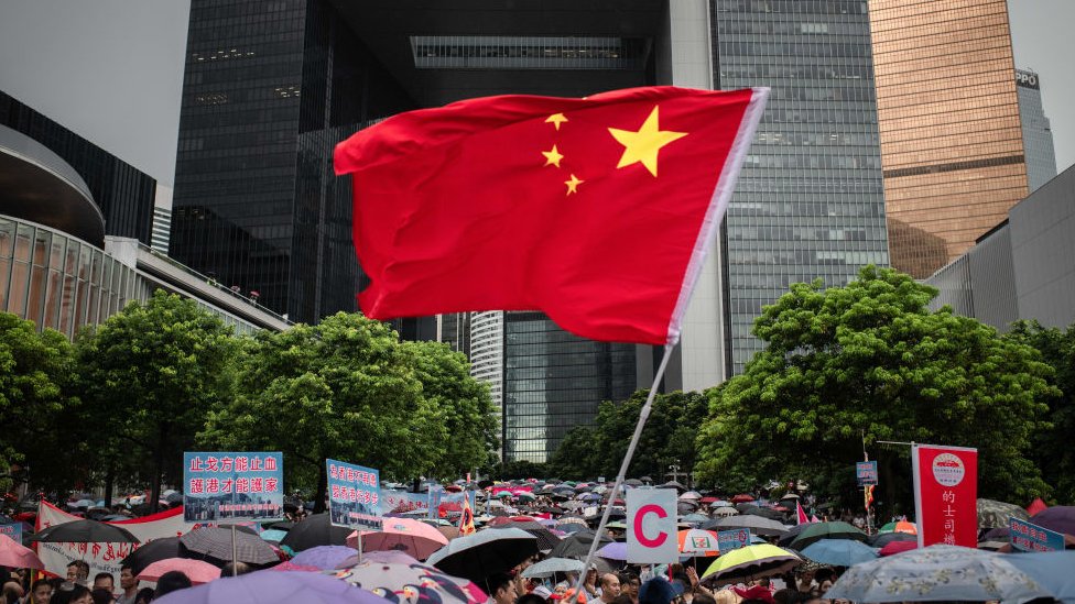 Китайский флаг развевается среди зонтиков на проправительственном митинге Safeguard Hong Kong в парке Тамар