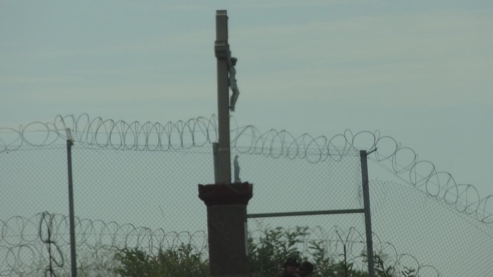 Статуя Христа на распятии, видимая с венгерской стороны границы, над колючей проволокой
