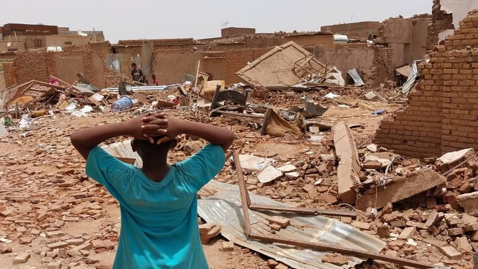 طفل يقف أمام المباني المتضررة بعد القتال في السودان