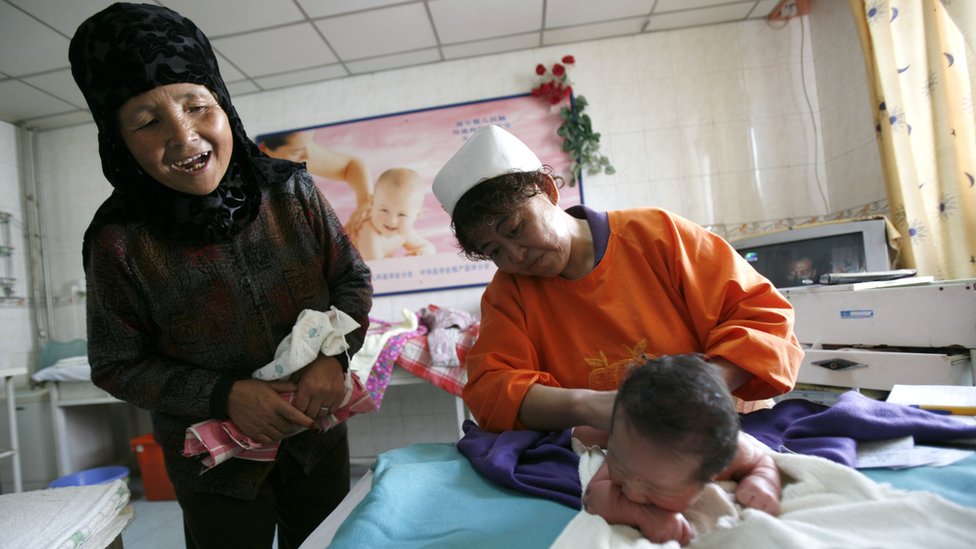 Una mujer con ropa tradicional observa a su nieto nacido en 2007 recibiendo un masaje de una enfermera en la provincia china de Qinghai
