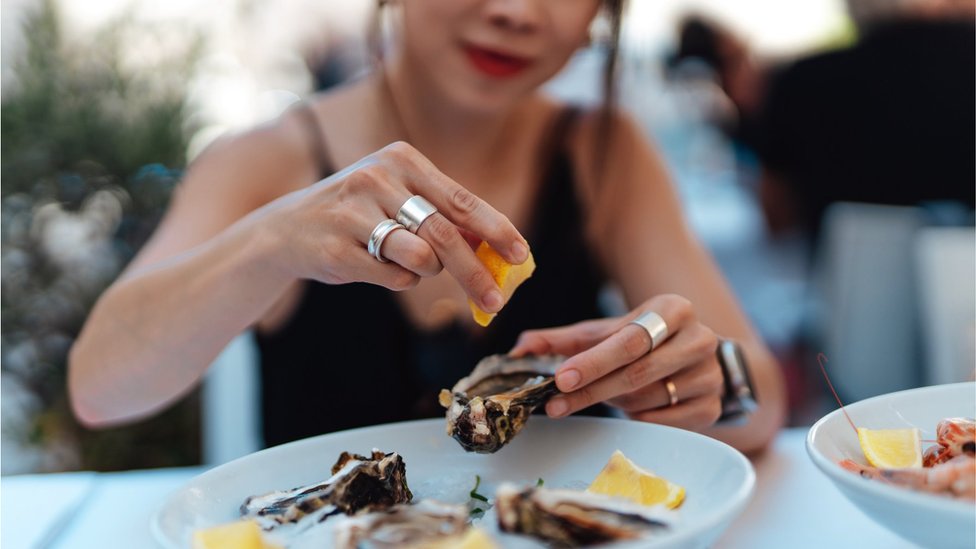 A woman squeezes lemon on an oyster