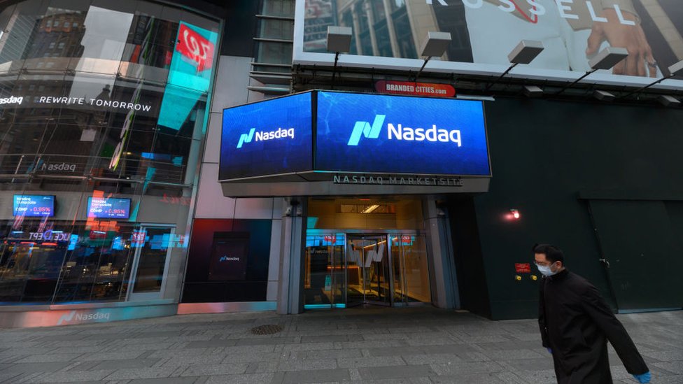 Мужчина в маске проходит мимо фондовой биржи Nasdaq в Нью-Йорке