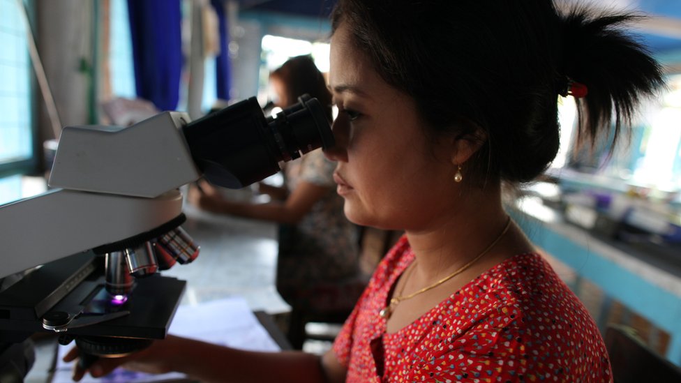 Бирманская женщина смотрит в микроскоп в лаборатории.
