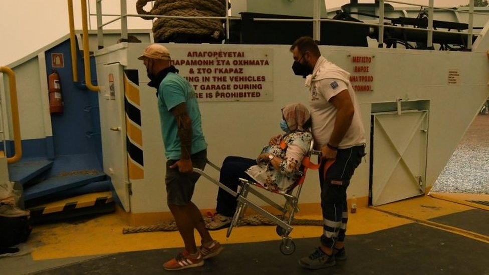 Locals carry a woman on board a ferry at the port of the village of Pefki