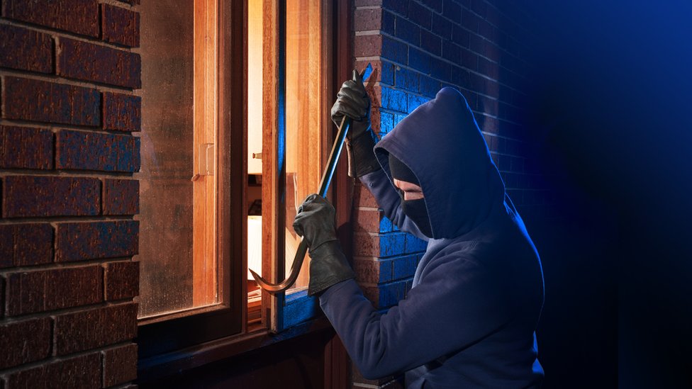 Ladrón intentando entrar a una casa forzando la ventana