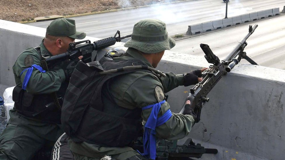 Militares con brazaletes azules apuntan sus armas Militares con brazaletes azules apuntan sus armas