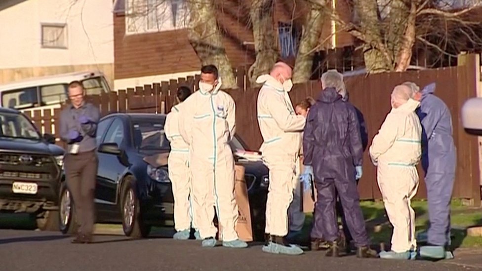 Police and investigators in bodysuits gather outside a suburban home where the victims were found in suitcases