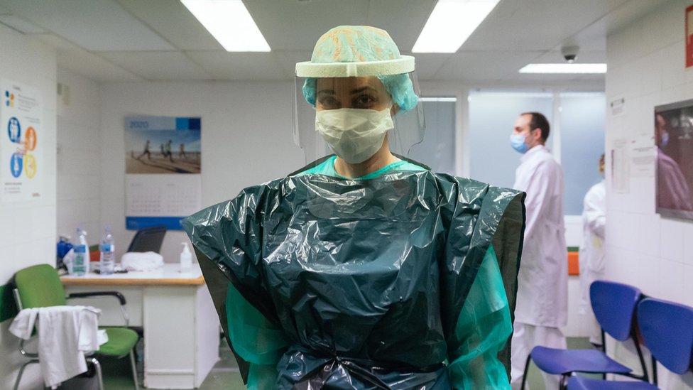 Also short of PPE, an intensive care nurse in Spain wears a bin bag and a protective plastic mask, donated by a local company.