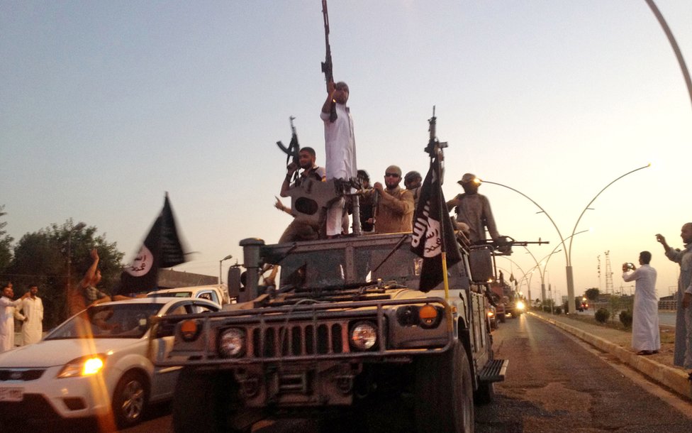 Fighters from the Islamic State group parade in a commandeered Iraqi security forces armoured vehicle down a main road at the northern city of Mosul, Iraq