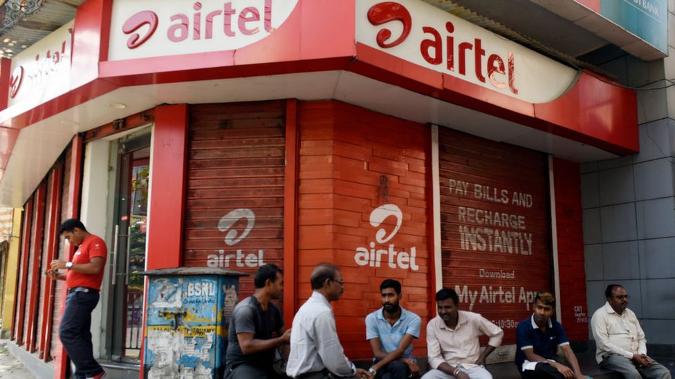 Мужчины сидят перед магазином Airtel в Калькутте