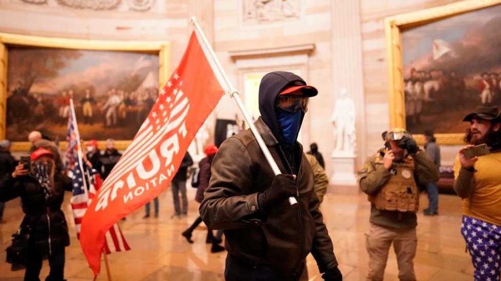 أحد المشاغبين يحمل علم ترامب داخل قاعة بالمبنى.