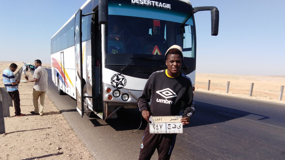 Элвин Жаката держит номерной знак тренера в пустыне по пути из Судана в Египет