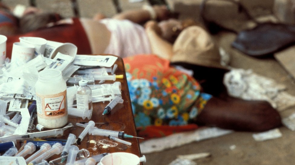 Photograph of medical by-products and syringes in focus, with people lying down visible in foreground