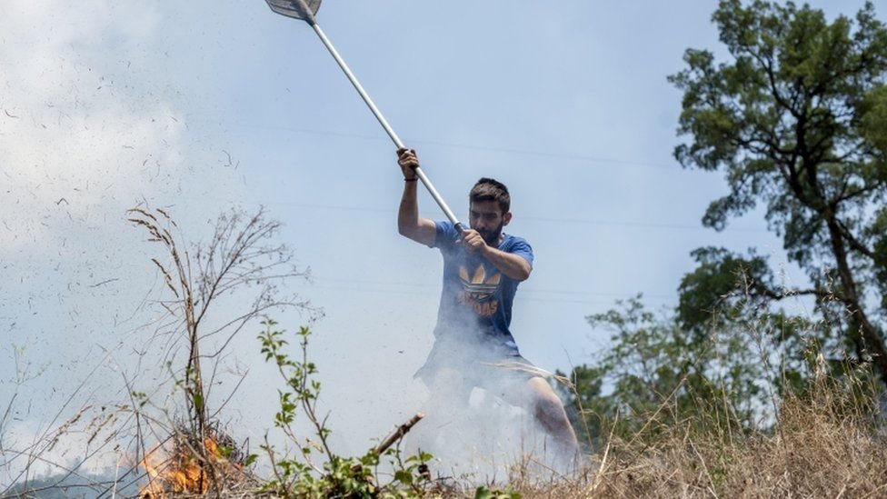 رجل يحاول إطفاء ألسنة اللهب باستخدام مكنسة في غاليسيا في 19 يوليو/تموز