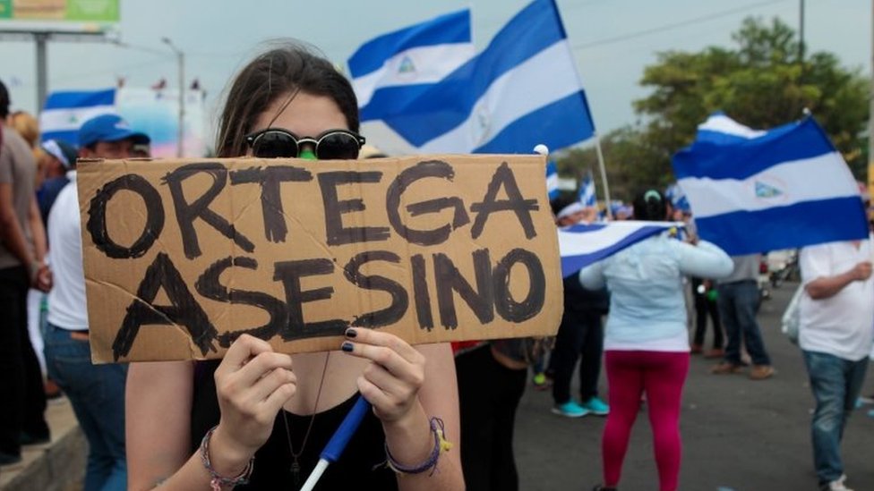 Демонстрант держит табличку с надписью «Убийца Ортеги» во время марша протеста против правительства президента Никарагуа Даниэля Ортеги в Манагуа, Никарагуа, 9 мая 2018 г.
