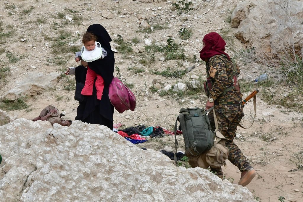 أحد أفراد قوات سوريا الديمقراطية يساعد إحدى عائلات مسلحي التنظيم على الخروج من بلدة باغوز في محافظة دير الزور شرقي سوريا. 14 مارس/آذار 2019