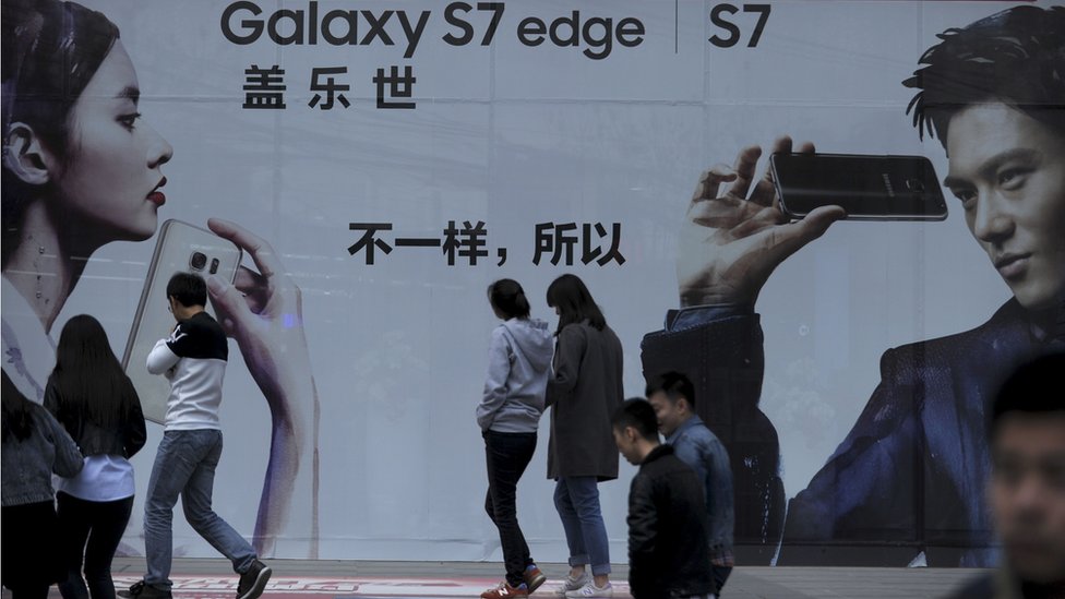 Люди проходят мимо плаката у входа в торговый центр в Пекине