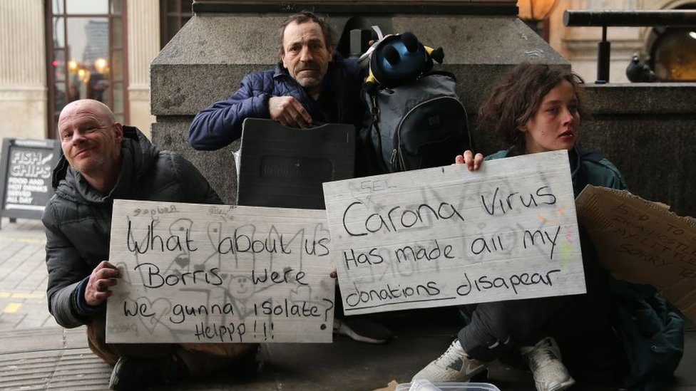 Бездомные люди держат таблички с надписью «А что насчет нас, Борис - мы были изолированы? Помогите!» И «Из-за вируса короны все мои пожертвования исчезли»