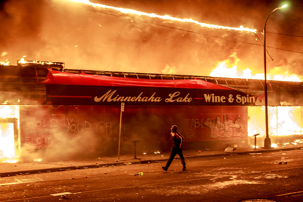 A man walks past a liquor store in flames