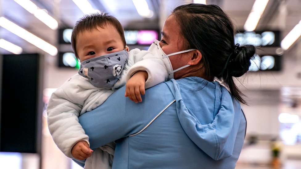 Woman holding a baby wearing a face mask