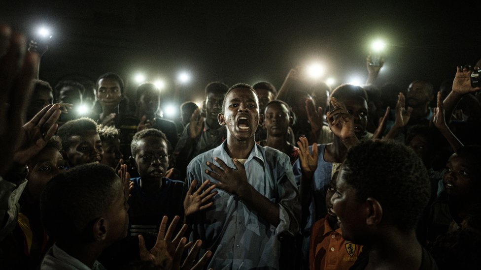 Un joven, iluminado por teléfonos móviles, recita un poema mientras los manifestantes cantan consignas pidiendo un gobierno civil, durante un apagón en Jartum (Sudán), el 19 de junio de 2019. Un joven, iluminado por teléfonos móviles, recita un poema mientras los manifestantes cantan consignas pidiendo un gobierno civil, durante un apagón en Jartum (Sudán), el 19 de junio de 2019.