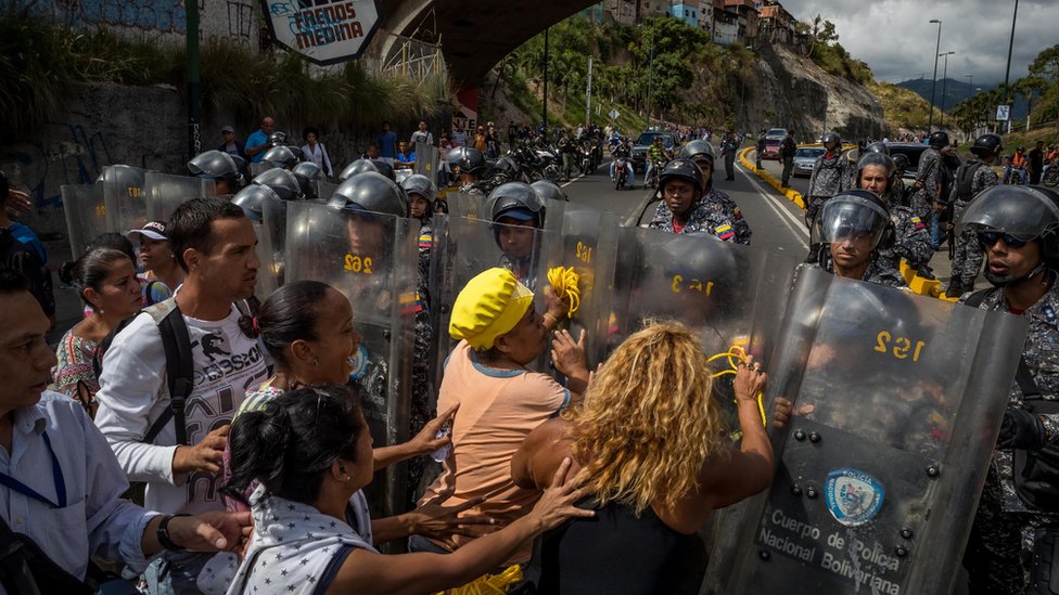 Группа людей протестует перед сотрудниками Боливарианской национальной полиции (PNB) в Каракасе, Венесуэла, 28 декабря 2017 года.