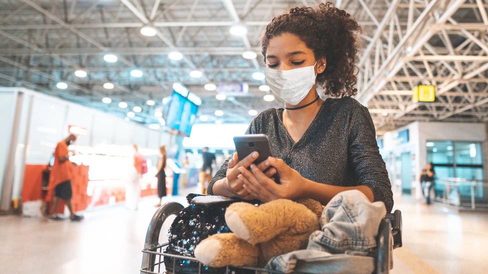 Девушка смотрит в свой телефон в аэропорту (стоковое изображение)
