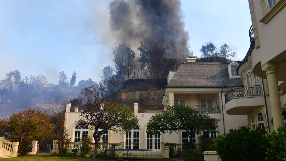 Огромный столб черного дыма поднимается от горящего дома на вершине холма рядом с домом, который все еще стоит в Бель-Эйр, к востоку от автострады 405, 6 декабря 2017 года в Лос-Анджелесе, Калифорния