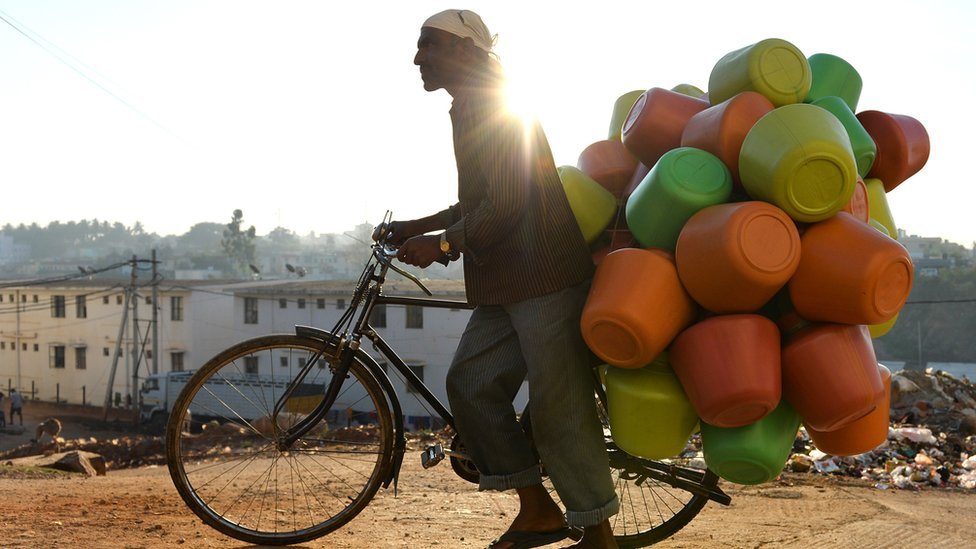 На этой фотографии, сделанной в марте 2015 года, изображен продавец, который несет на своем велосипеде разноцветные пластиковые горшки с водой для продажи домашним хозяйствам в Бангалоре.