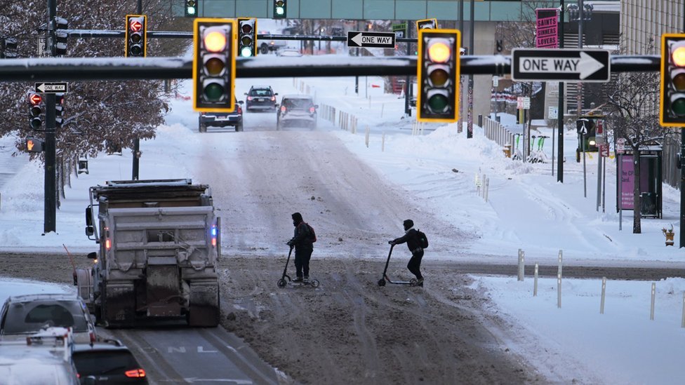 Dois homens atravessam uma rua coberta de neve em Denver, Colorado, em meio a uma forte tempestade de inverno em 22 de dezembro de 2022