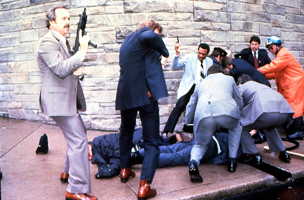 Vista de los agentes del Servicio Secreto armados alrededor de los cuerpos del policía Thomas K Delahanty y del Secretario de Prensa de la Casa Blanca James Brady mientras el sospechoso del tiroteo, John Hinckley Jr, es detenido (a la derecha) fuera del Hotel Washington Hilton, Washington DC, 30 de marzo de 1981.