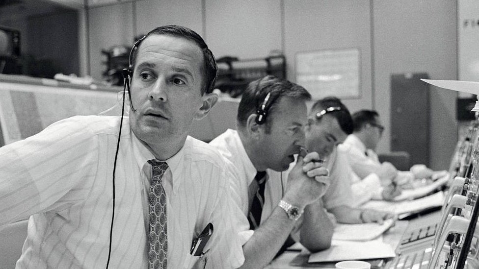 Personal en tierra sentados frente a consolas durante la misión del Apolo 11