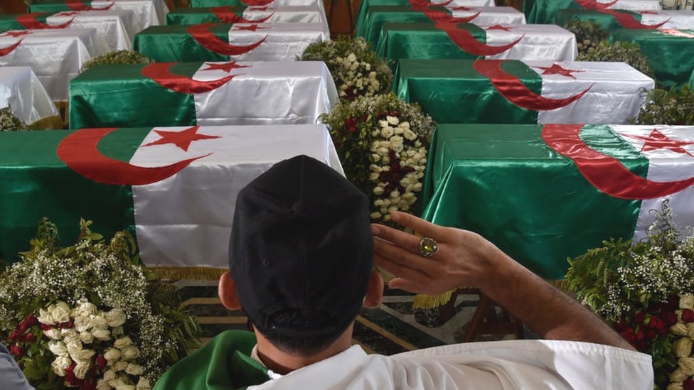 Мужчина из Алжира отдает дань уважения перед гробами, задрапированными национальным флагом, с останками 24 алжирских бойцов сопротивления во Дворце культуры Муфди Закария через день после того, как они были доставлены из Франции - июль 2020 года