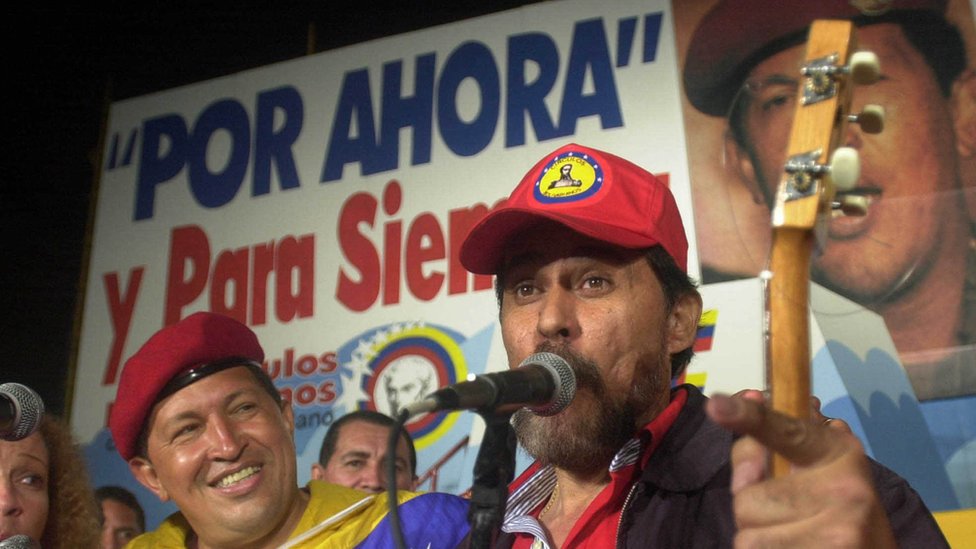 Hugo Chávez ante un cartel en el que se lee *Por ahora y para siempre*
