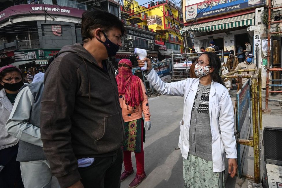 A volunteer (R) checks the temperature of devotees who arrive to take a holy dip in the waters of the River Ganges during Makar Sankranti, a day considered to be of great religious significance in the Hindu mythology, on the first day of the religious Kumbh Mela festival in Haridwar on 14 January 2021