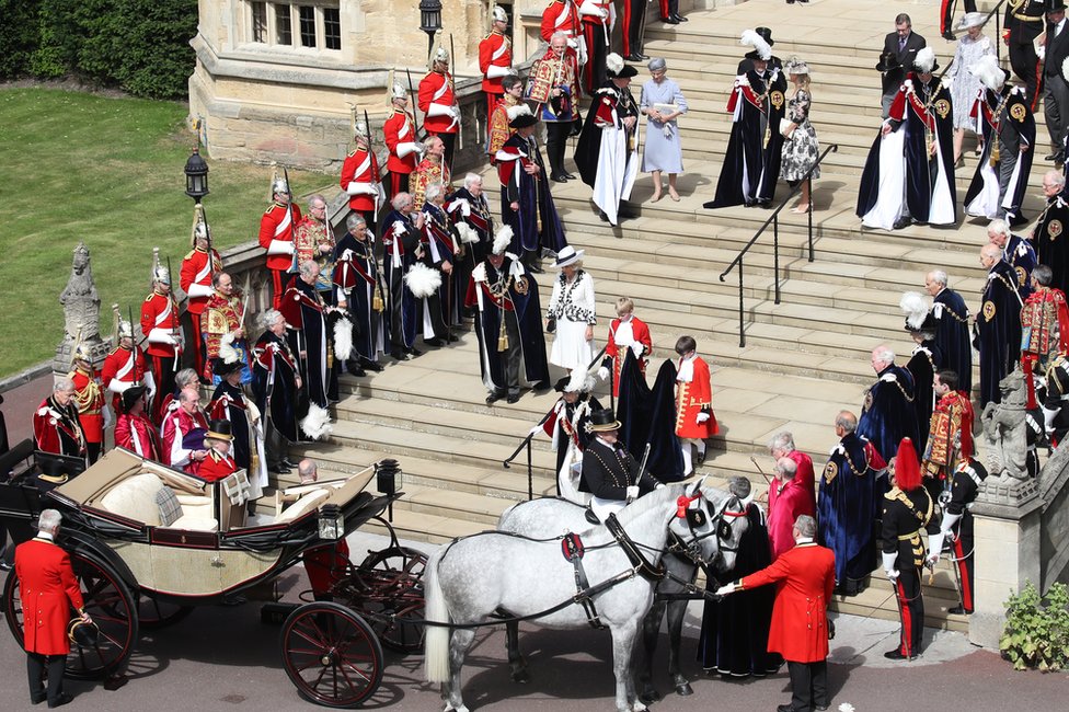 Охранники, военные, другие члены Королевской семьи и Рыцари Подвязки наблюдают, как королева Елизавета II спускается по ступеням к своей карете во время Ордена Подвязки в Виндзорском замке