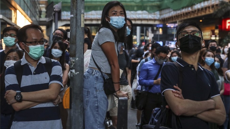 Демонстранты демонстративно носят маски для лица после того, как законодательный орган принял чрезвычайные меры, запрещающие их