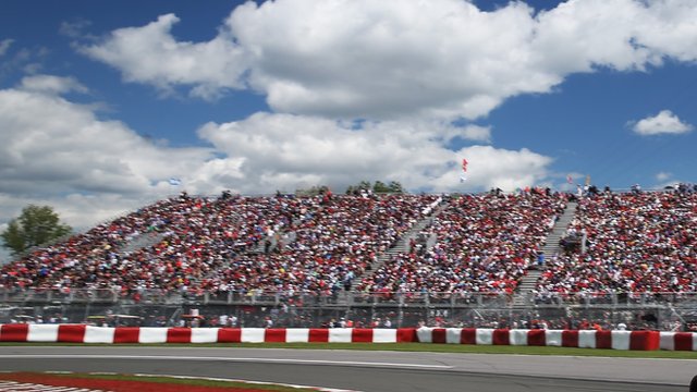 Spectators sit by the F1 track in Montreal. Blue skies and white clouds are overhead.