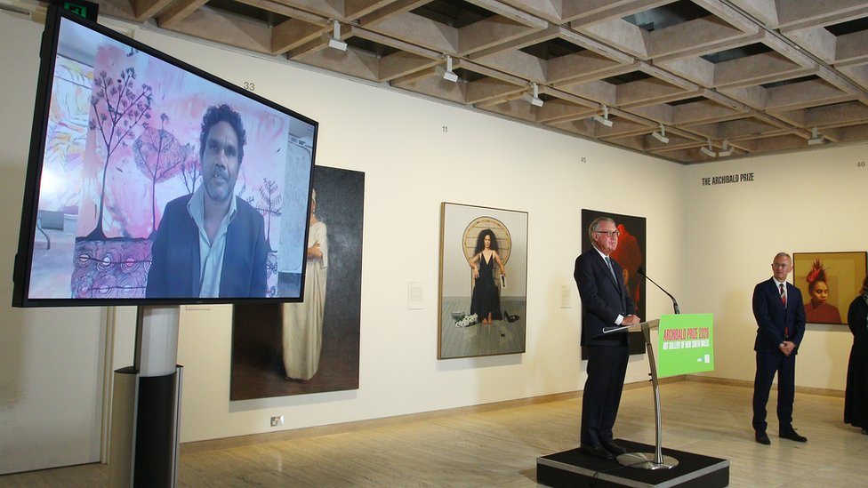 Винсент Наматжира на экране позади директора галереи Майкла Брэнда при объявлении приза