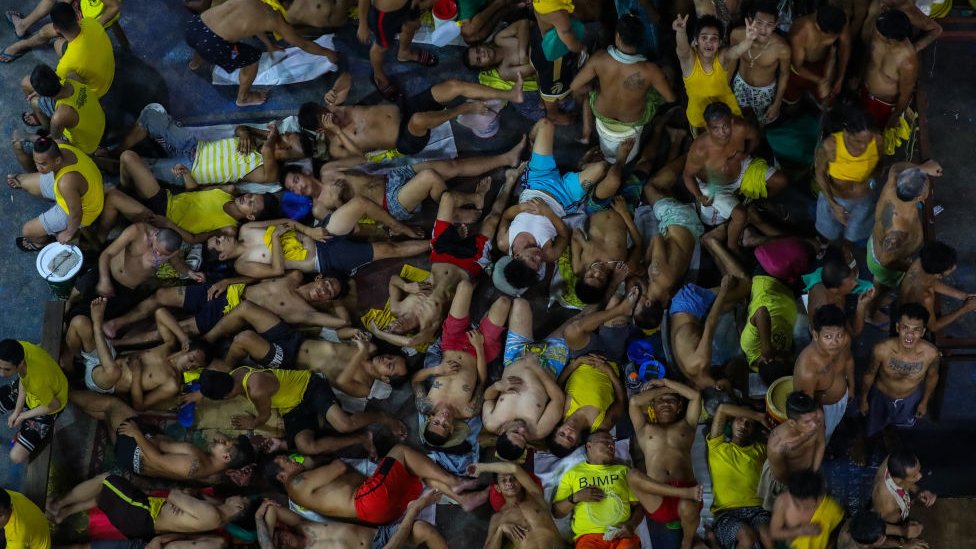 На этой фотографии, сделанной 27 марта 2020 года, показаны заключенные, спящие и жестикулирующие в тесноте в переполненном дворе тюрьмы Кесон-Сити