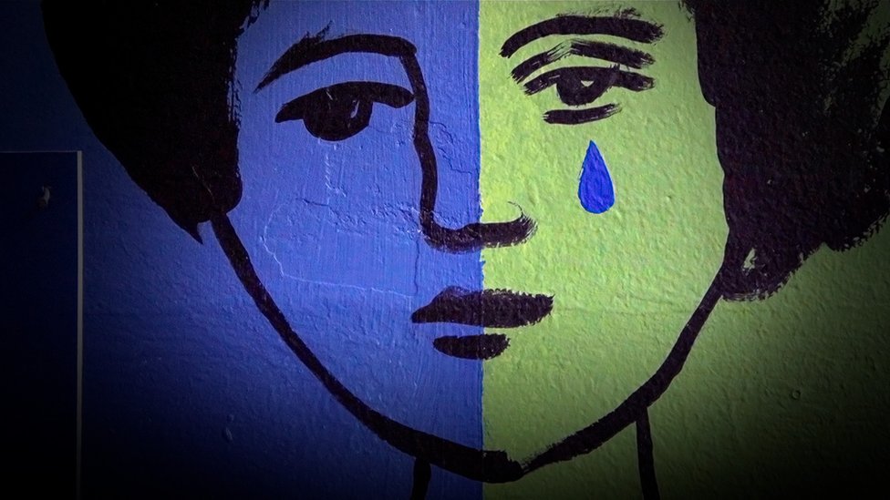 Mural de una mujer con la cara verde y azul llorando