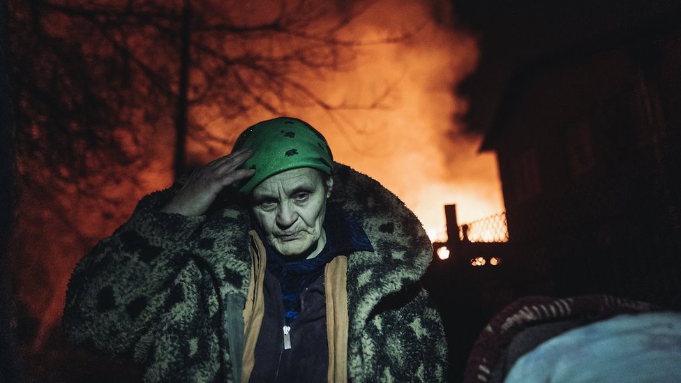 أوكراني أمام منازل محترقة بينما يطفئ عمال خدمة الطوارئ حريقاً بعد قصف على خط الجبهة في باخموت في إيفانيفسكي